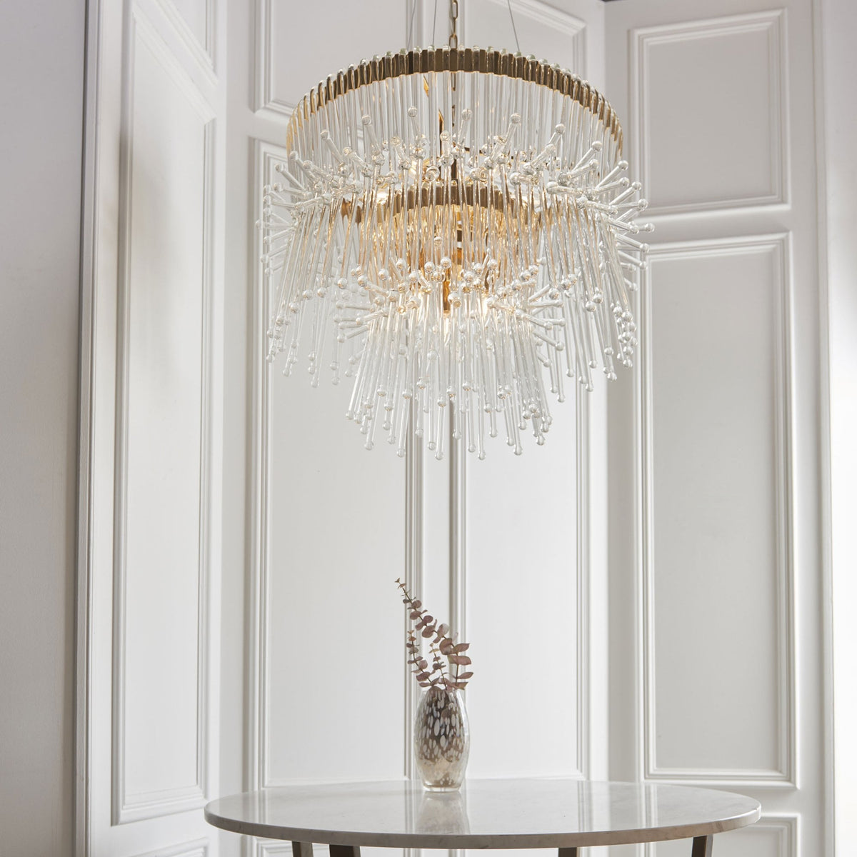 Elegant two-tier gold and clear glass chandelier hanging in a room with white paneled walls.