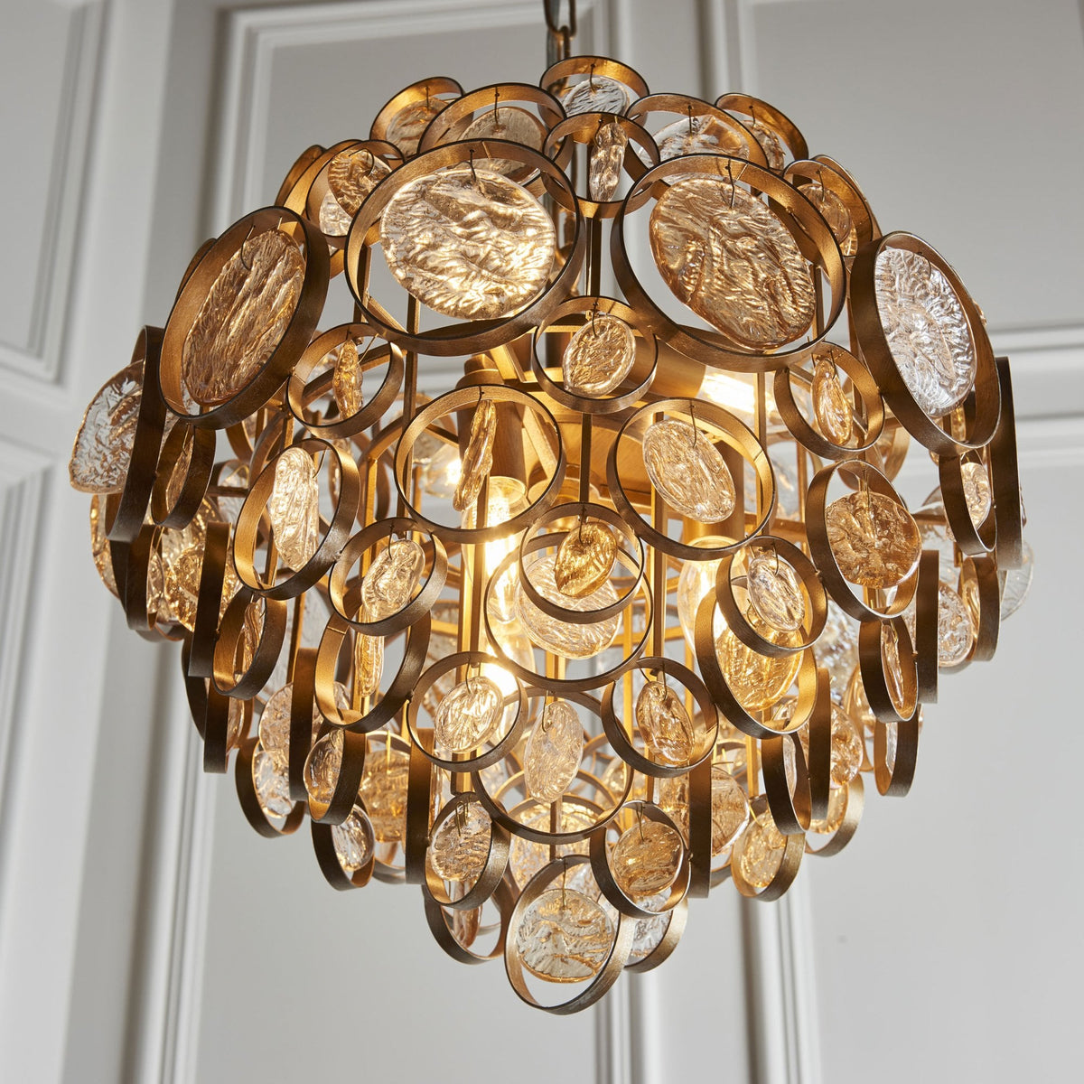 A close-up of a gold chandelier, featuring multiple textured glass discs, illuminates a warm glow.