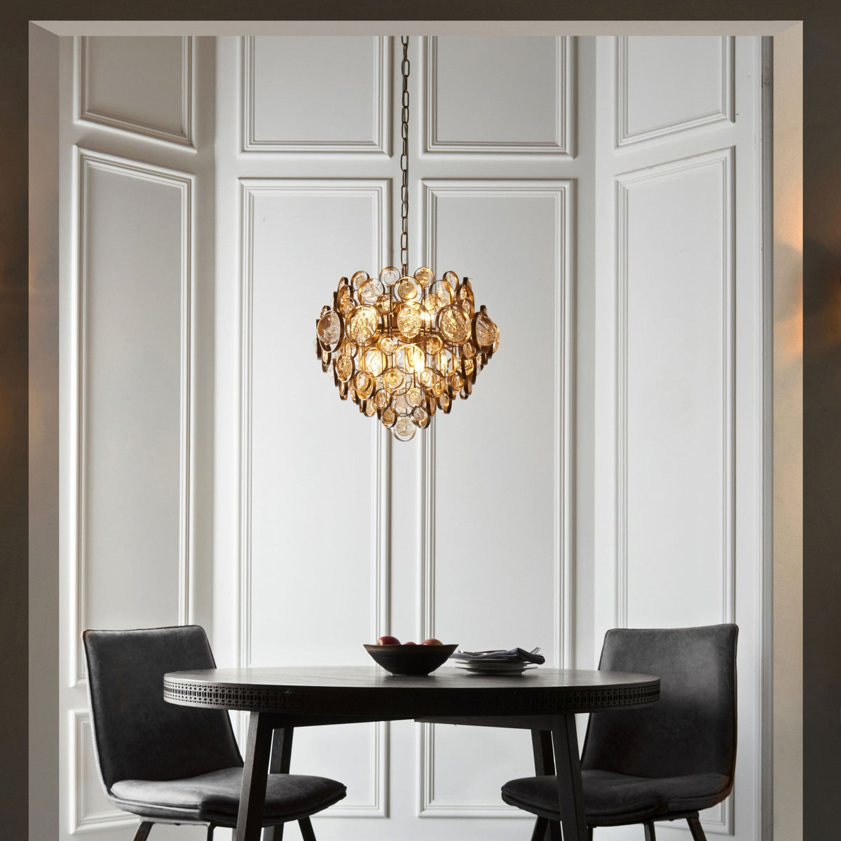 Gold chandelier illuminating a cozy dining nook with a round table and two chairs against white paneling.