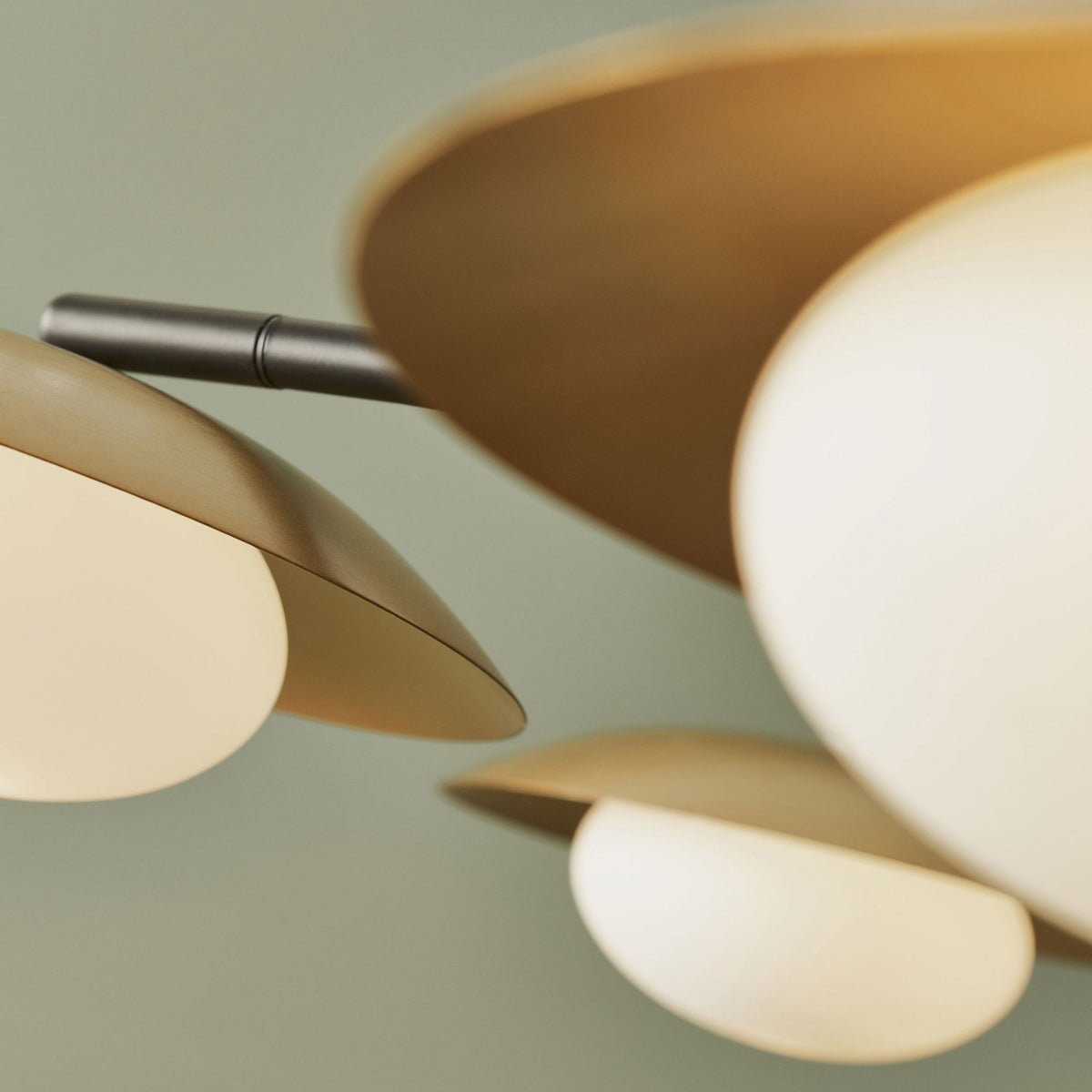 Close-up of a gold-toned, saucer-shaped light fixture with a white globe, part of a modern chandelier.