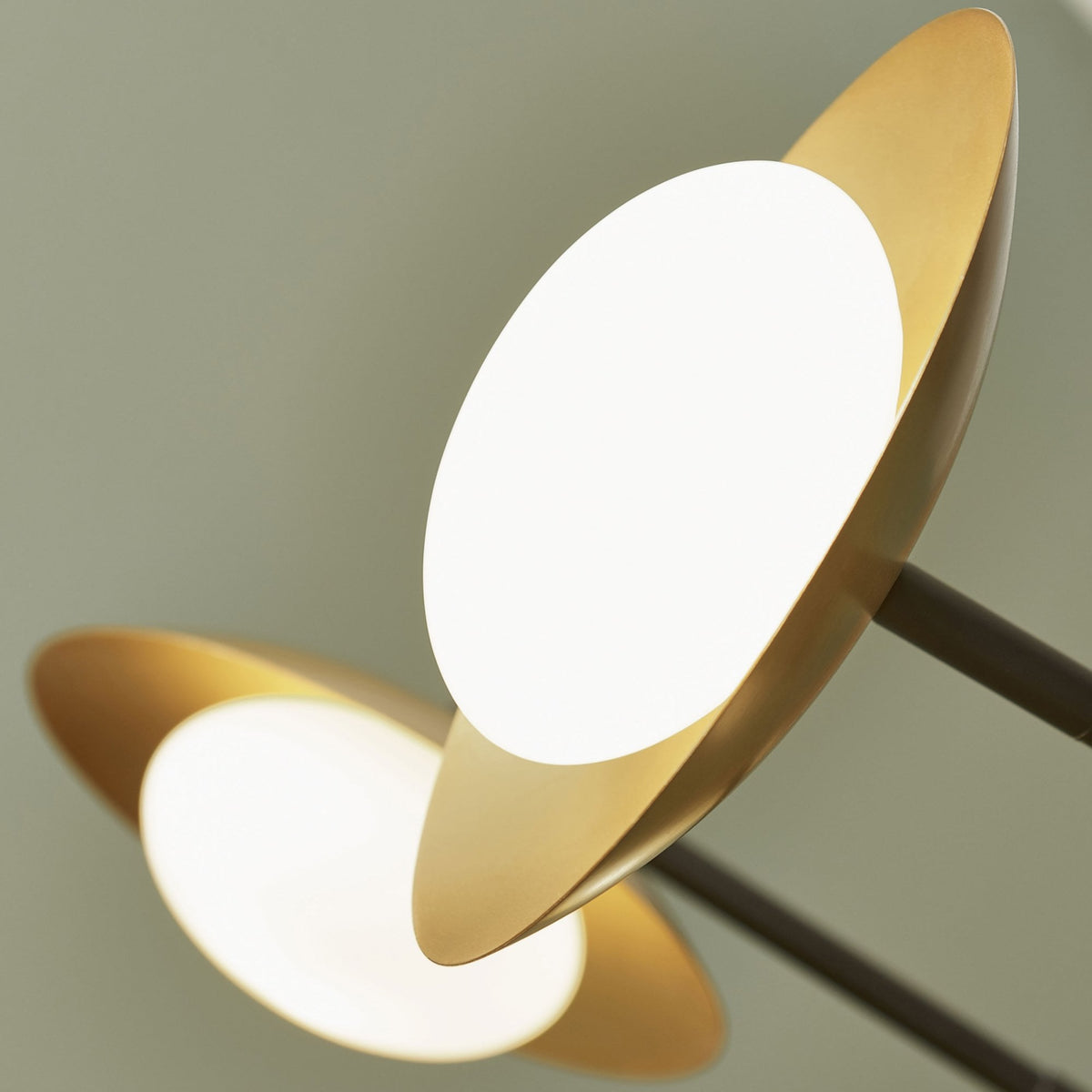 Close-up of two gold-toned, saucer-shaped light fixtures with glowing white globes on a light background.
