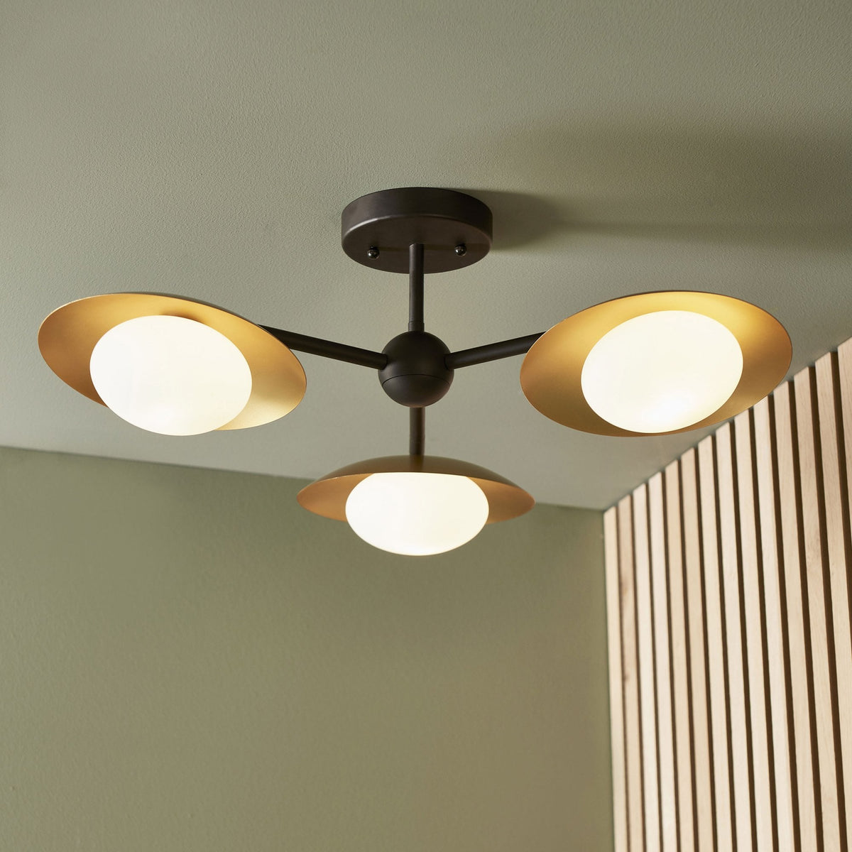 A sleek, modern ceiling light fixture with three spherical bulbs encased in gold-colored metal shades.