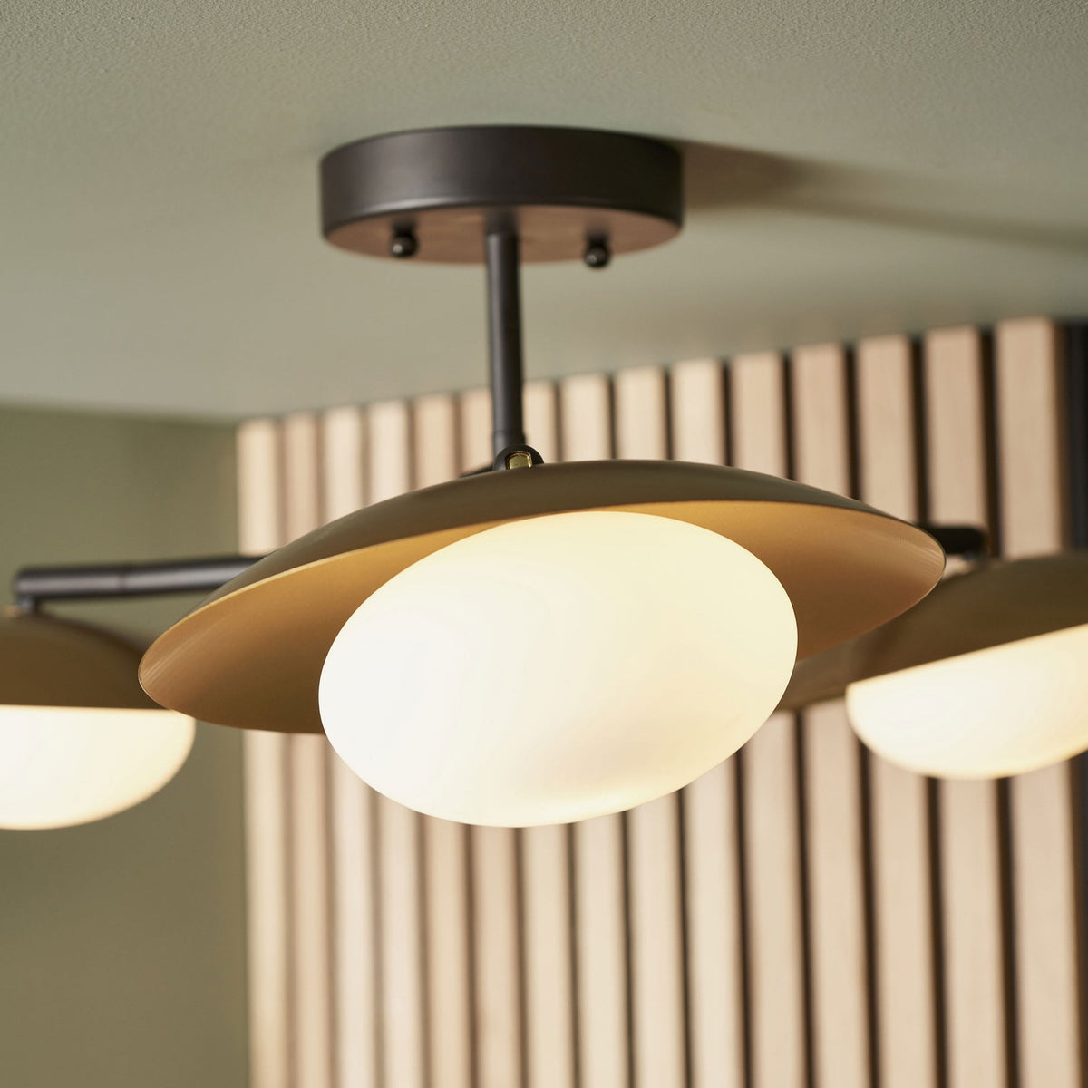 A close-up view of a modern ceiling light, showcasing one spherical bulb with its gold-colored metal shade.