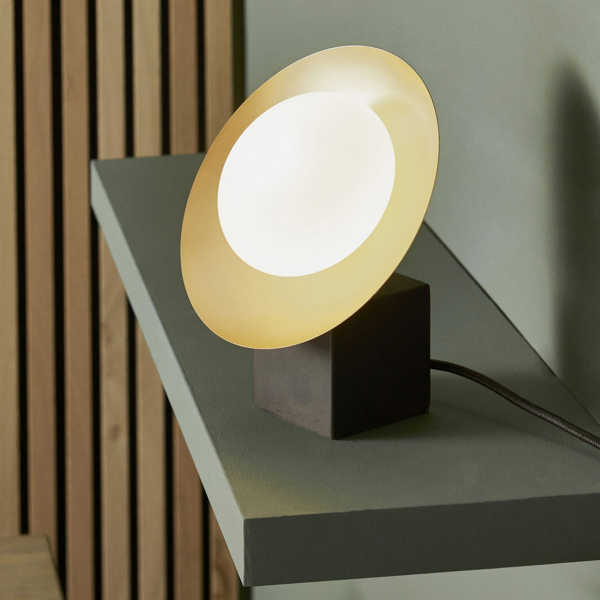 Table lamp with a dark base and a gold and white disc light source.