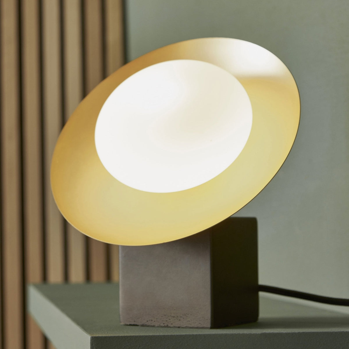 Table lamp with a dark base and a gold and white disc light source.