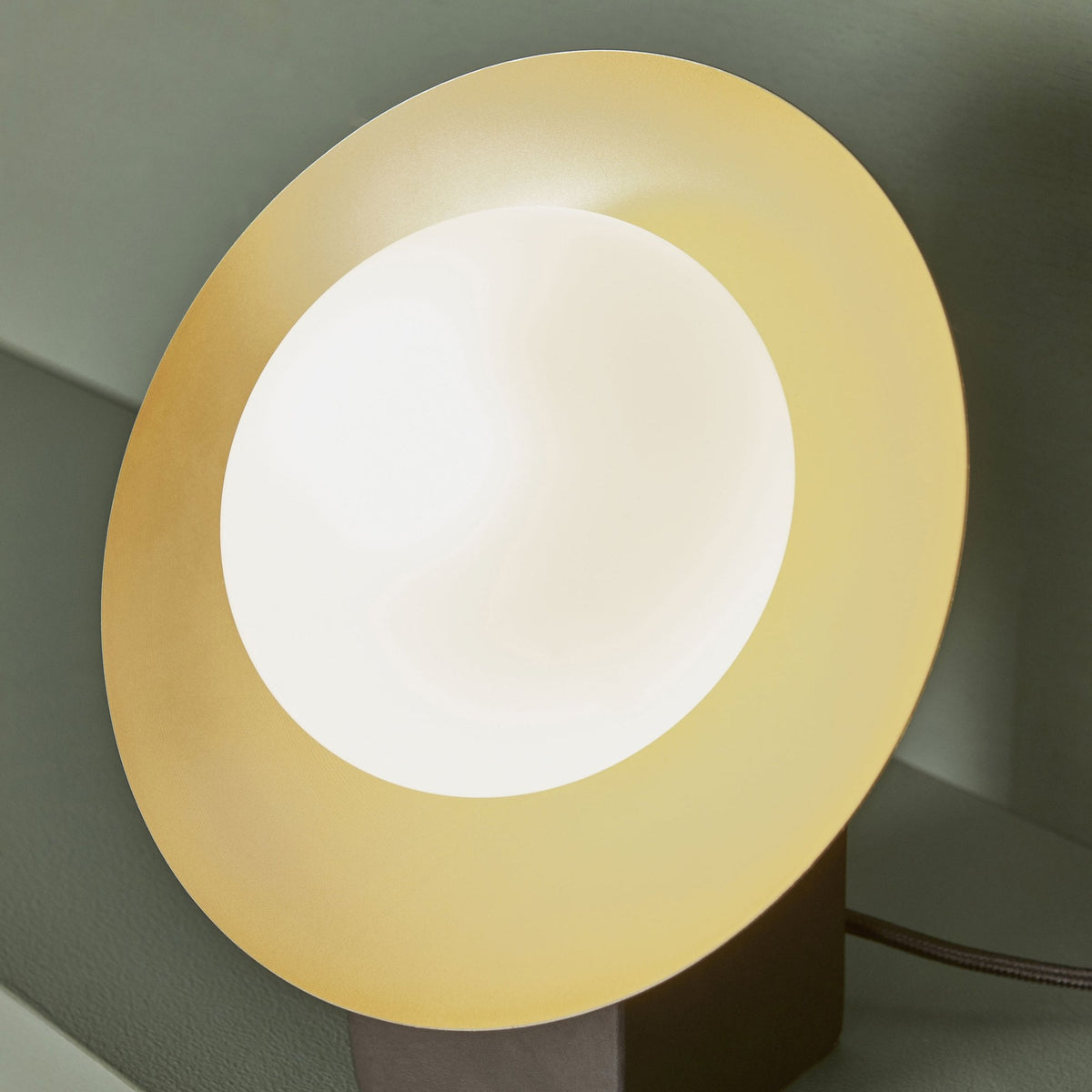 Close-up of a table lamp with a dark base and a gold and white disc light source.