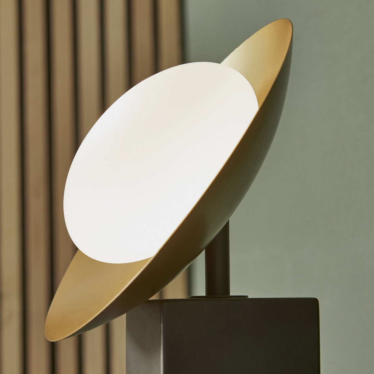 Close-up of a table lamp with a dark base and a gold and white disc light source.