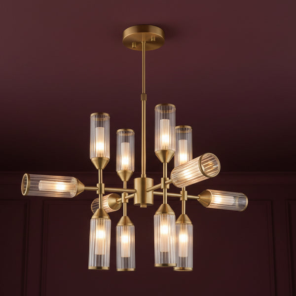 Un lustre moderne en laiton brossé à neuf lumières avec des abat-jour en verre cannelé, sur fond blanc.