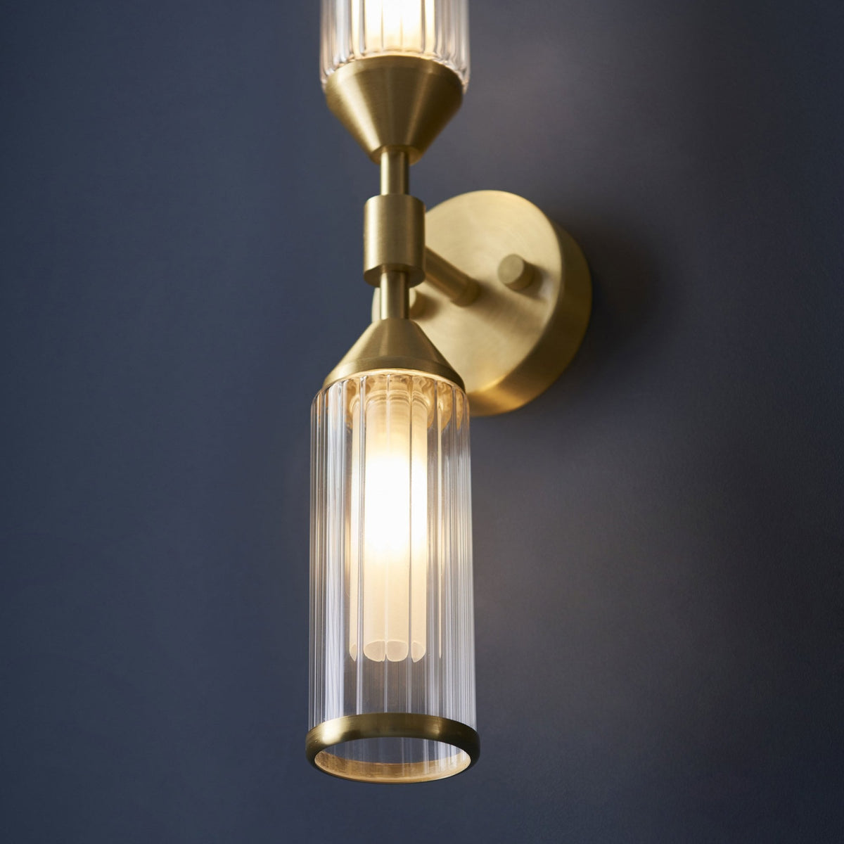 A close-up of the brass wall light showing the lower illuminated fluted glass shade.