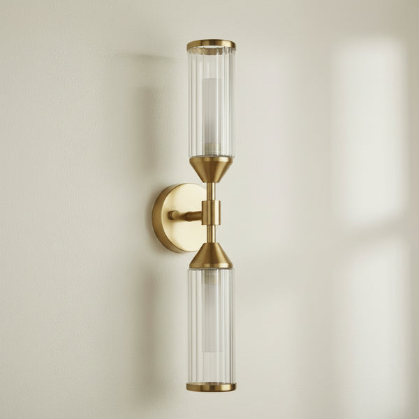 A brass wall sconce with two unlit ribbed glass shades, one pointing up and one down, on a white background.