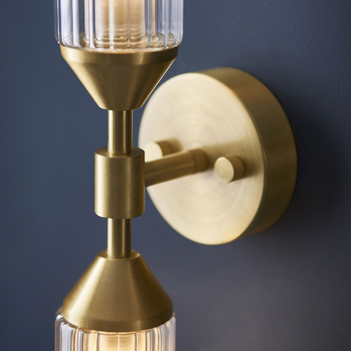 A close-up of the brass fixture of the wall light against a dark blue wall.