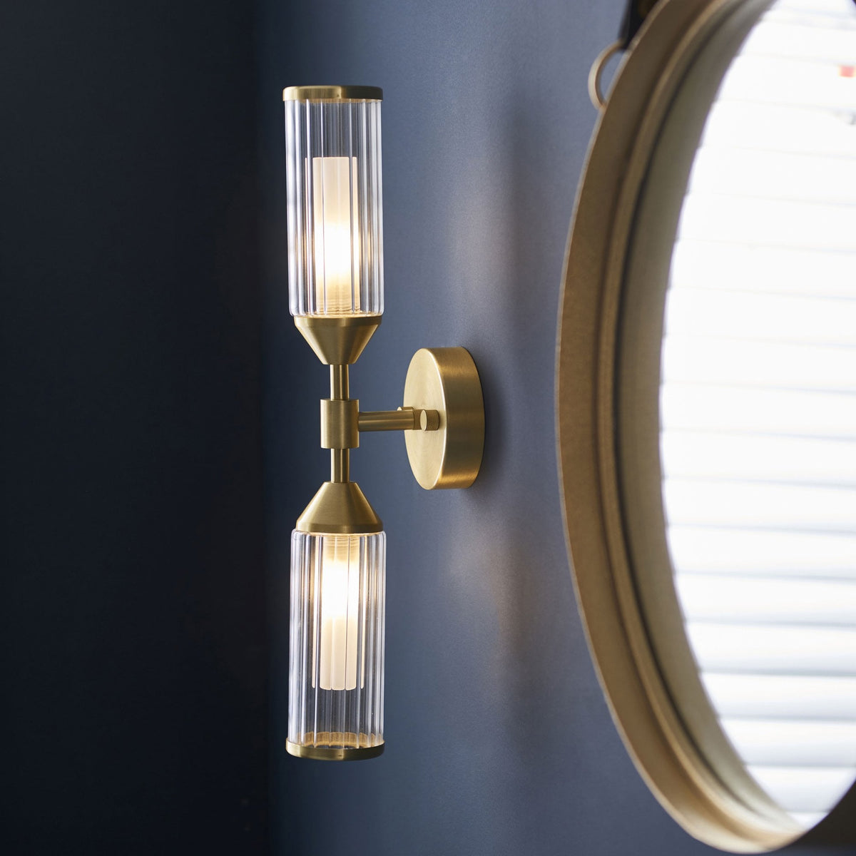 A brass wall light mounted next to a round mirror, casting a warm glow.