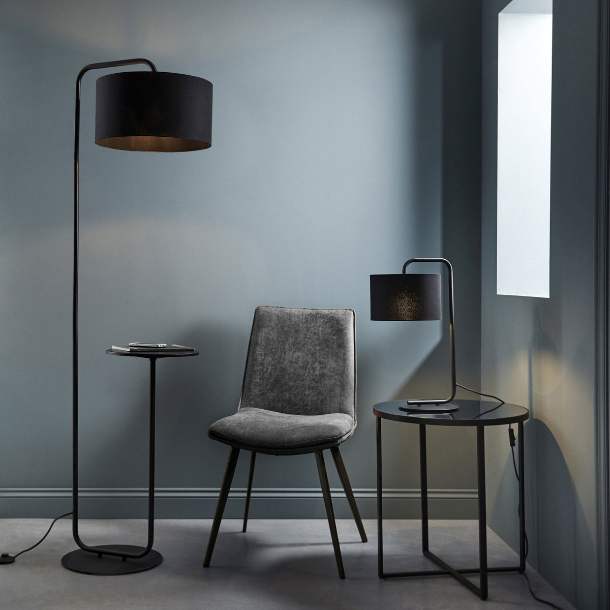 Black floor lamp with a side table, a grey chair, and a matching black table lamp on a round side table.