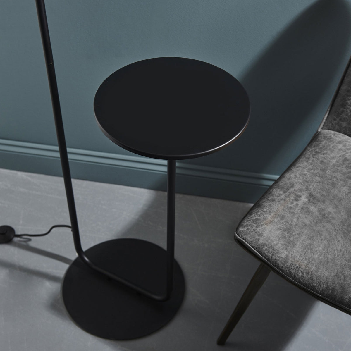 Close-up of the black round side table attached to the floor lamp, next to a grey chair.