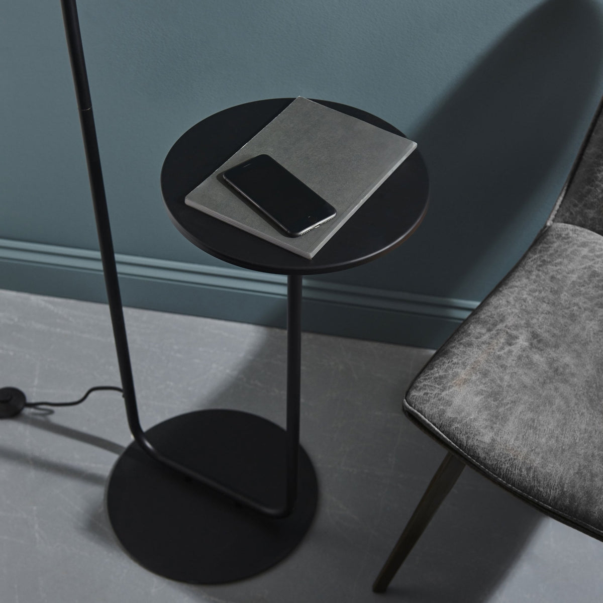 Close-up of the black round side table attached to the floor lamp, with a phone and notebook.