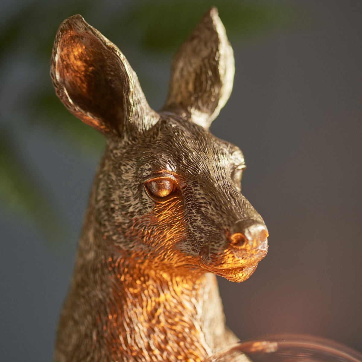 Close-up of the golden kangaroo lamp's head, illuminated by the warm glow of the bulb.