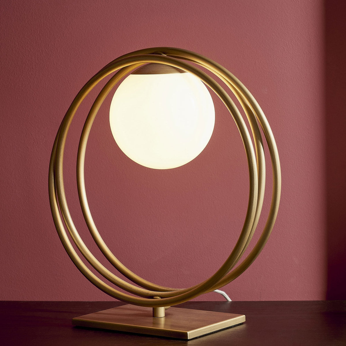 A modern desk lamp with a spherical light source surrounded by concentric golden rings.