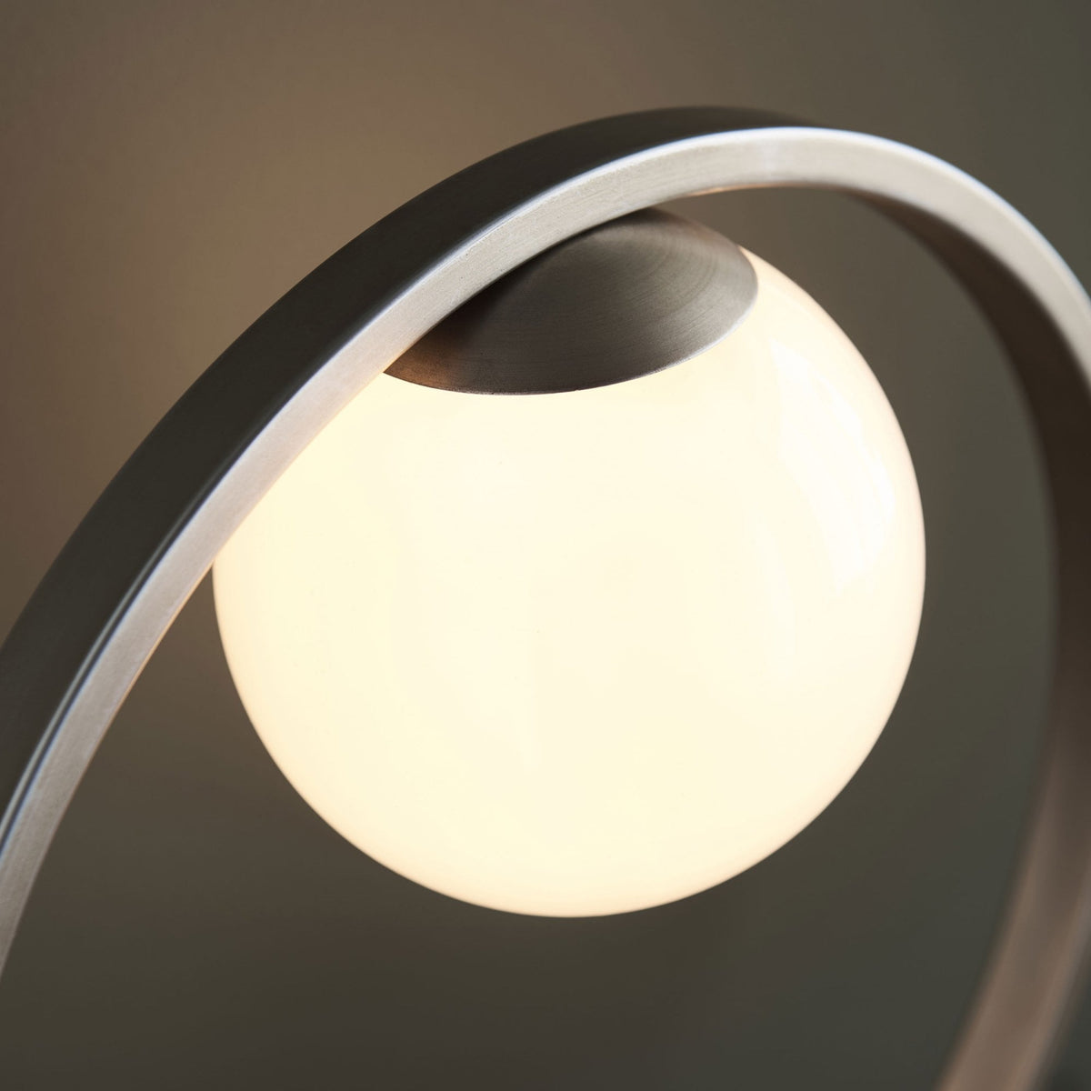 Close-up of the glowing spherical bulb and brushed metal frame of a modern table lamp.