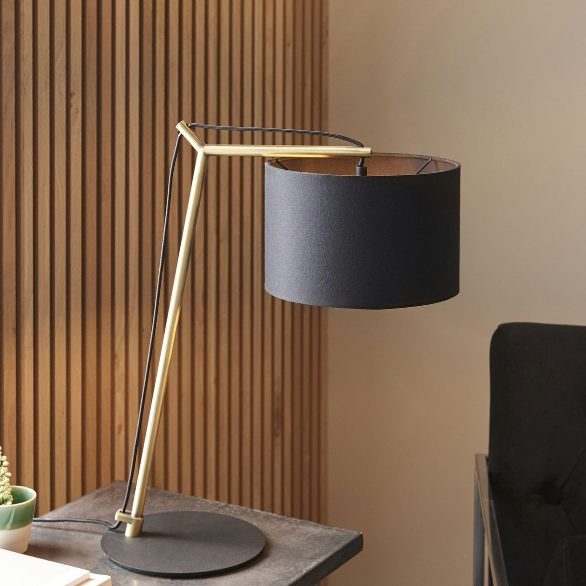 Modern desk lamp with a black shade and gold-colored frame on a dark wooden table.