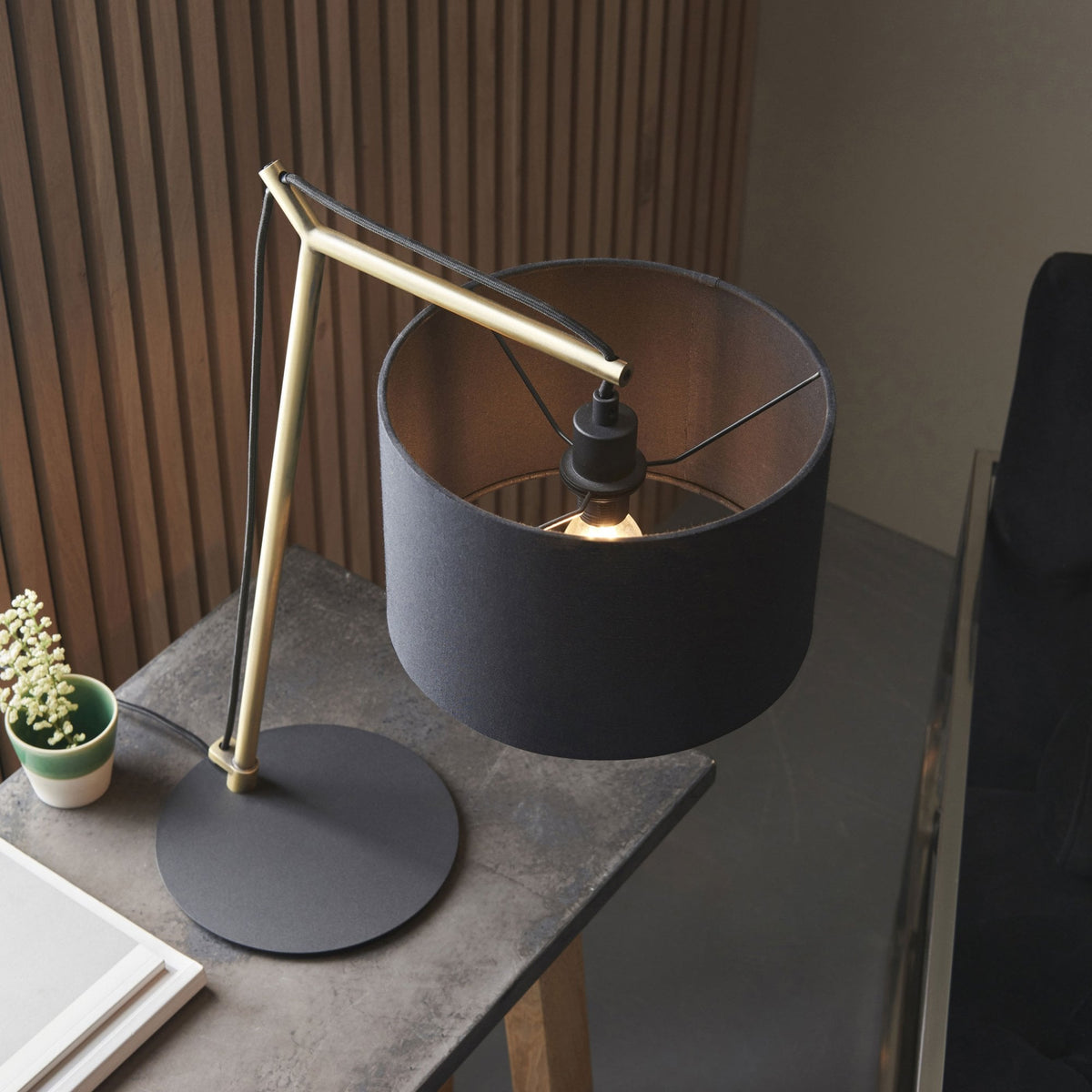 Overhead view of a modern desk lamp with a black shade and gold-colored frame, light on.