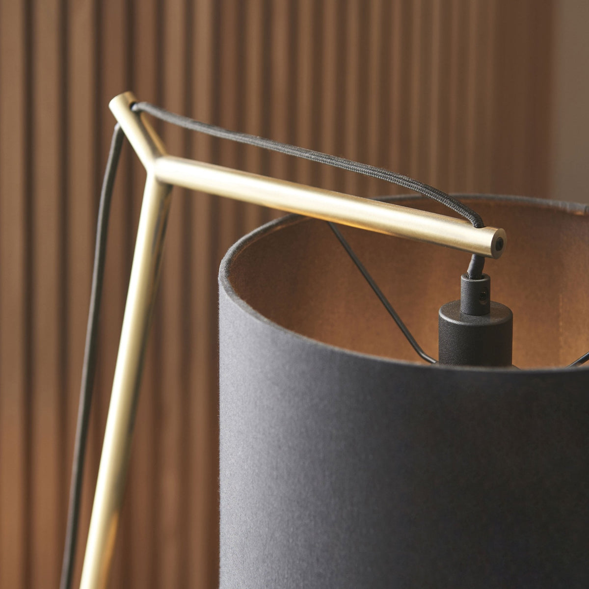 Close-up of the gold-colored frame and black shade of a modern desk lamp.