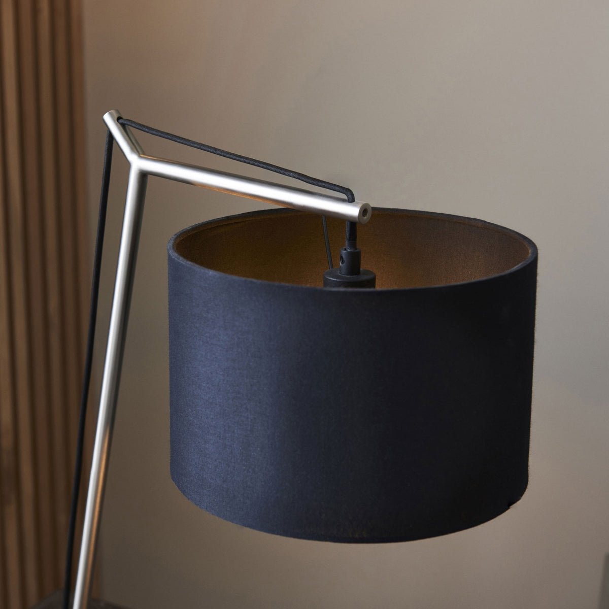 Close-up of a black and gold table lamp with a silver frame, against a light brown wall.
