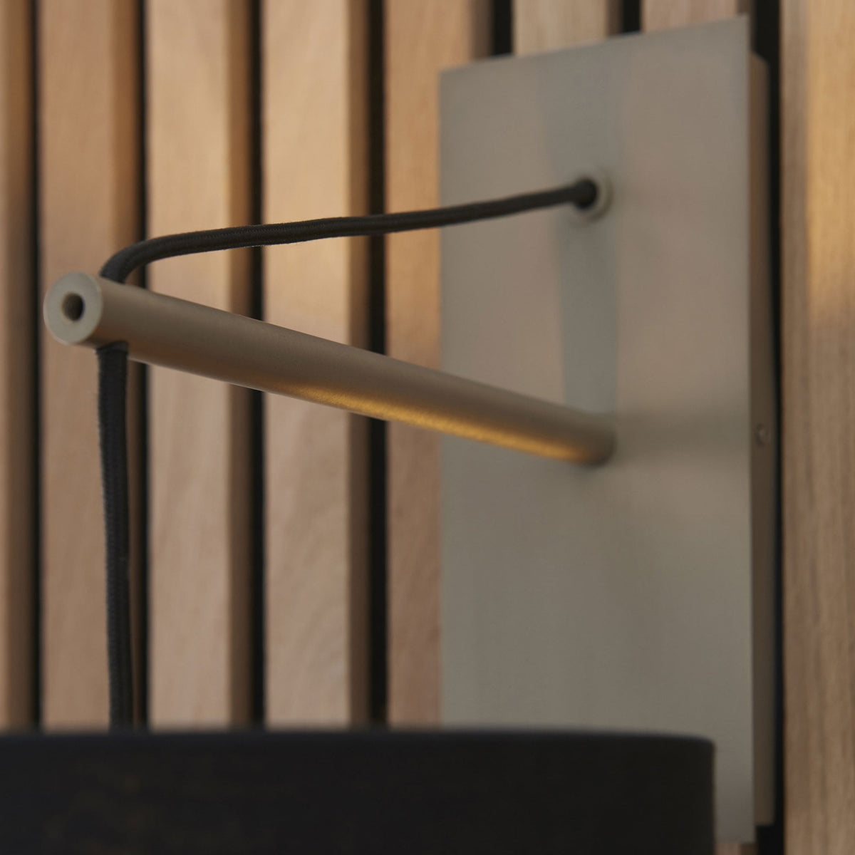 Close-up of the wooden arm and light grey backplate of a wall light, with a black drum shade below.