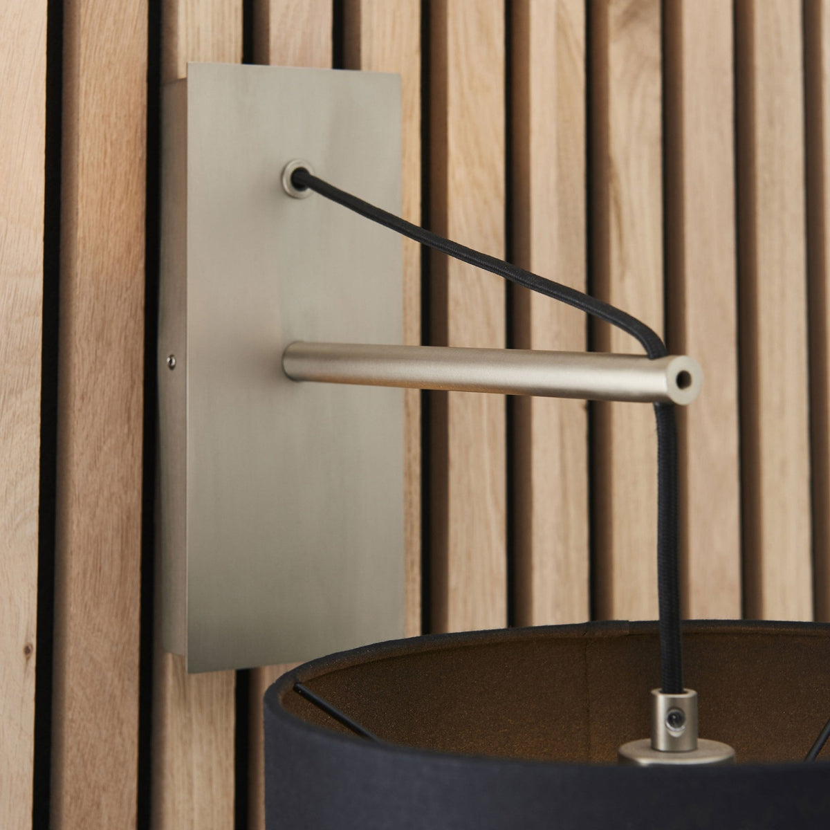 Close-up of the brushed steel arm and backplate of a wall light, with a black drum shade below.