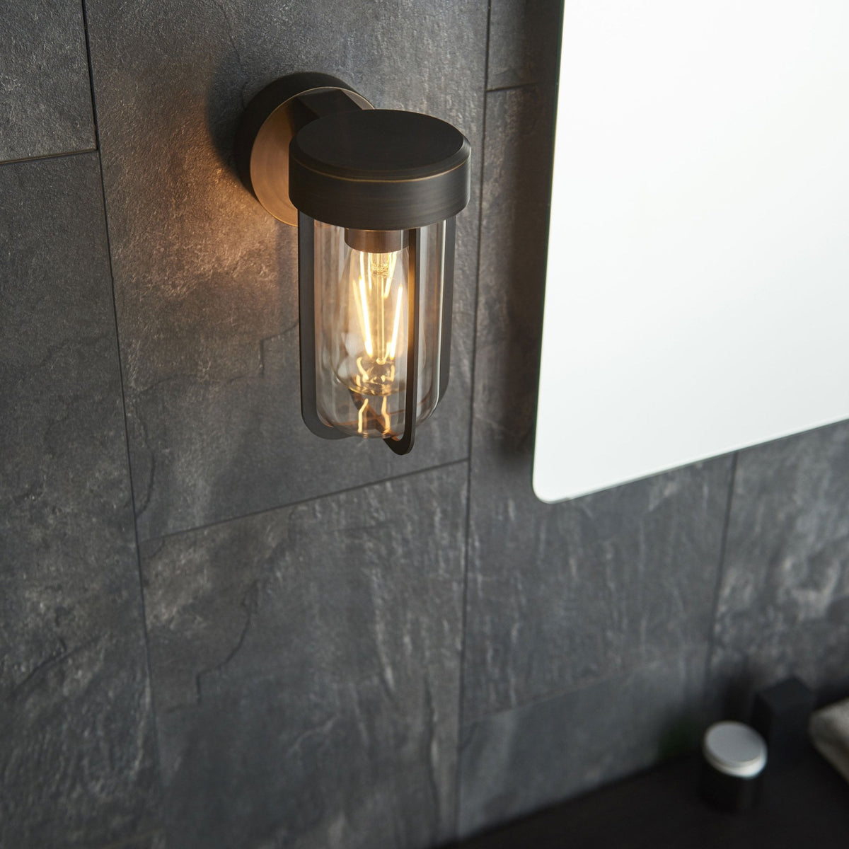 Applique murale noire pour l'extérieur ou la salle de bain, éclairant un mur carrelé sombre à côté d'un miroir.