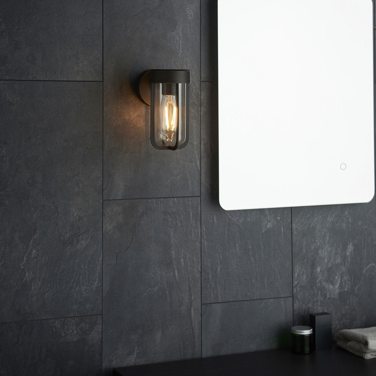 Applique murale noire pour l'extérieur ou la salle de bain, sur un mur carrelé sombre avec un miroir à côté.