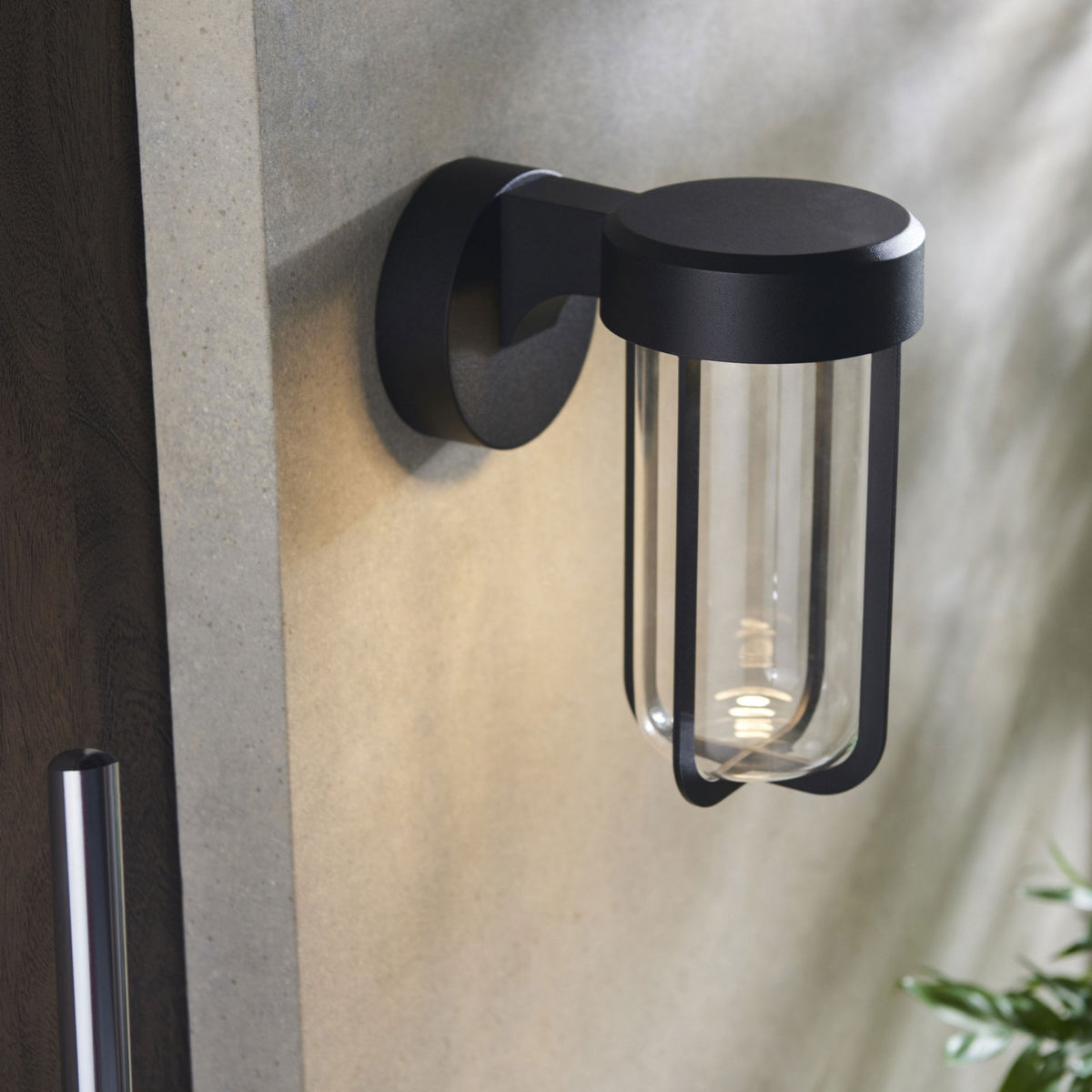 A close-up of a black outdoor wall light with a clear glass cylinder and exposed filament bulb.