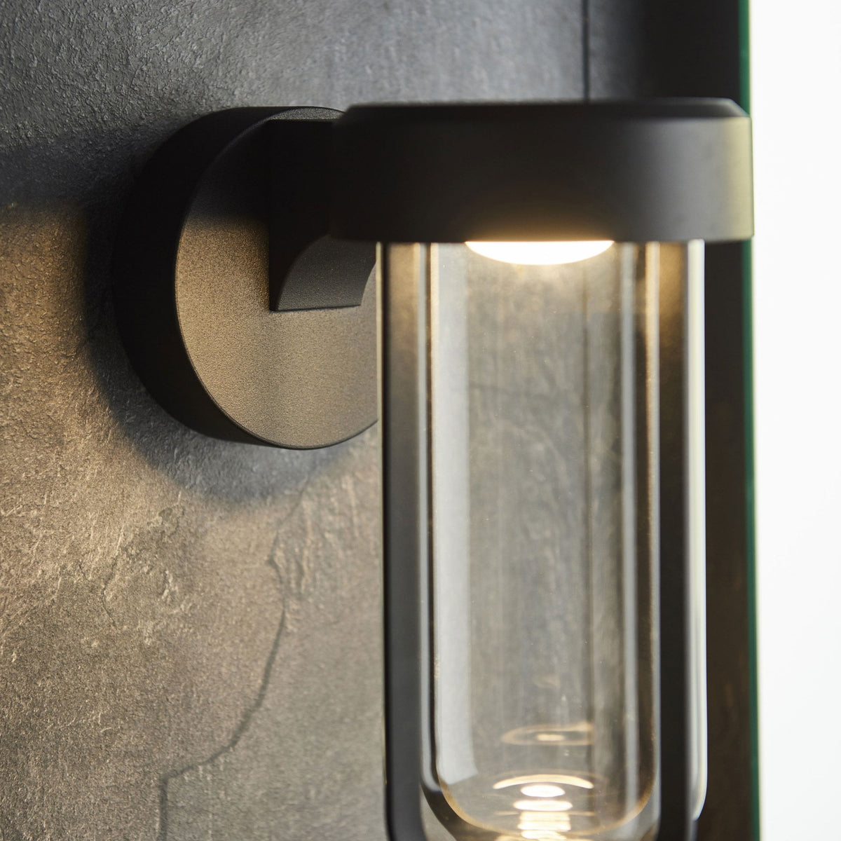 A close-up of the black outdoor wall light, showcasing the bright LED bulb inside the clear glass.