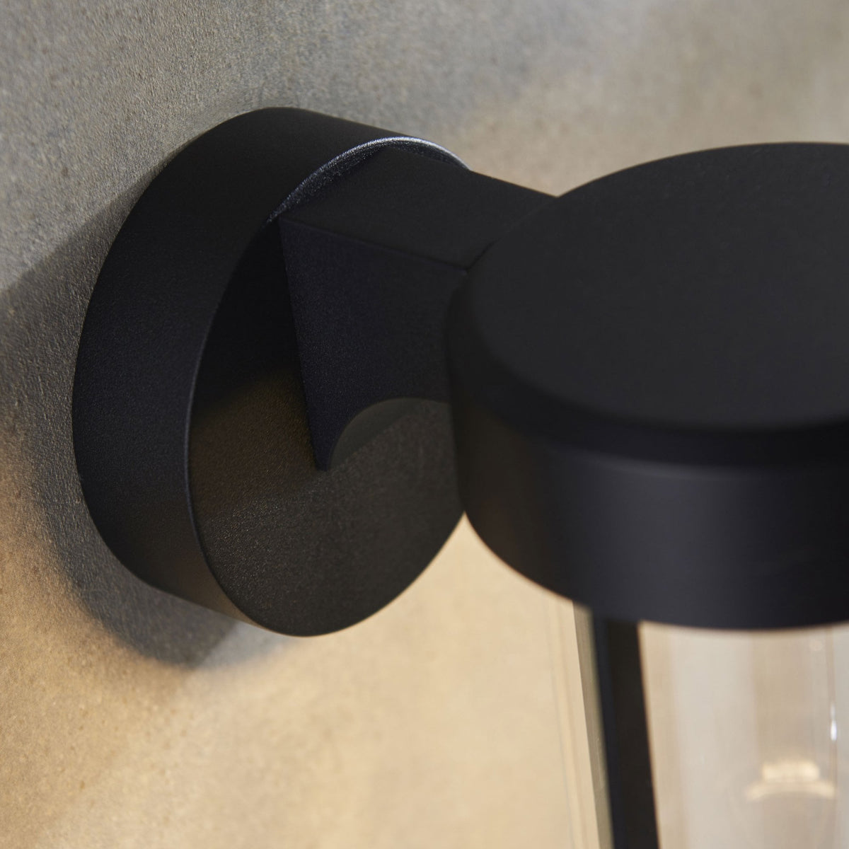A close-up of the matte black finish of the wall sconce's base and top cap, highlighting its texture.