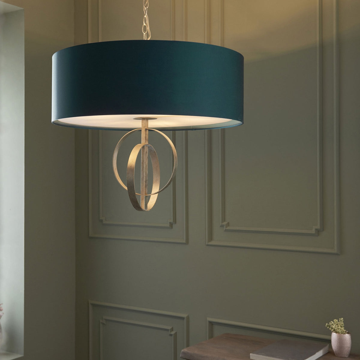 A teal drum shade pendant light with an openwork silver orbit design illuminates a sophisticated room.