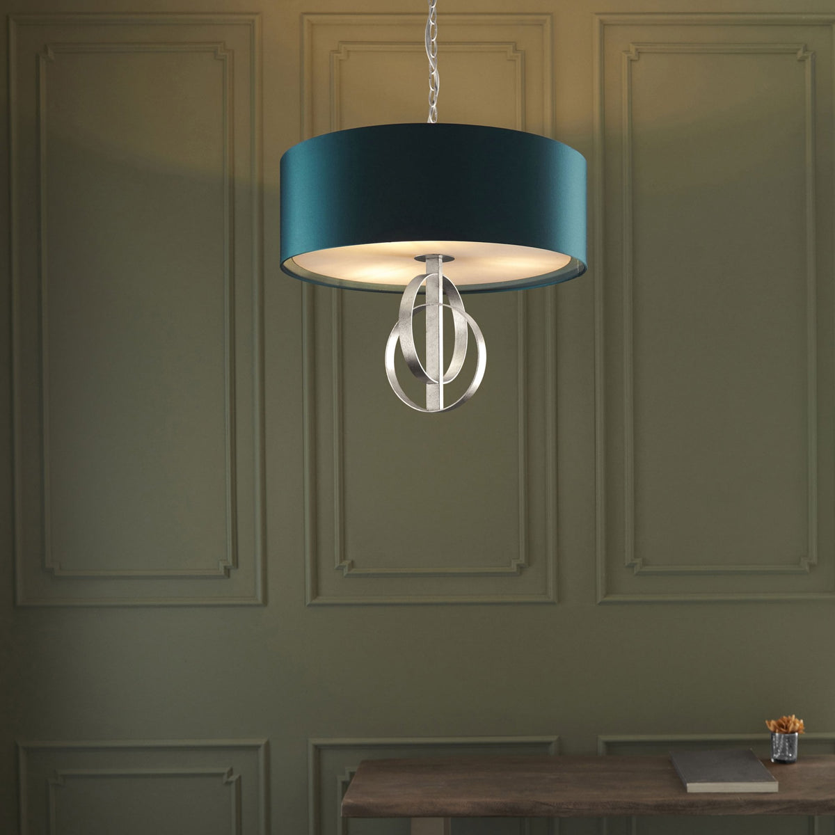 A modern pendant light with a teal shade and brushed silver accents hangs in a room with wainscoting.