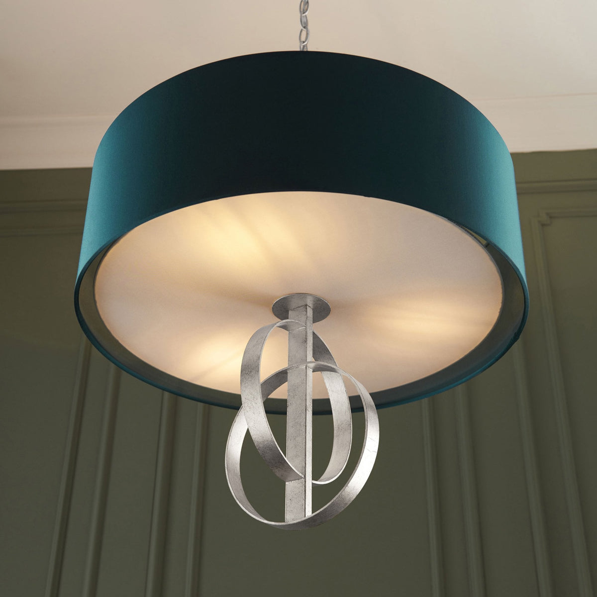 A close-up view of the illuminated teal pendant light, highlighting the brushed silver decorative rings below.