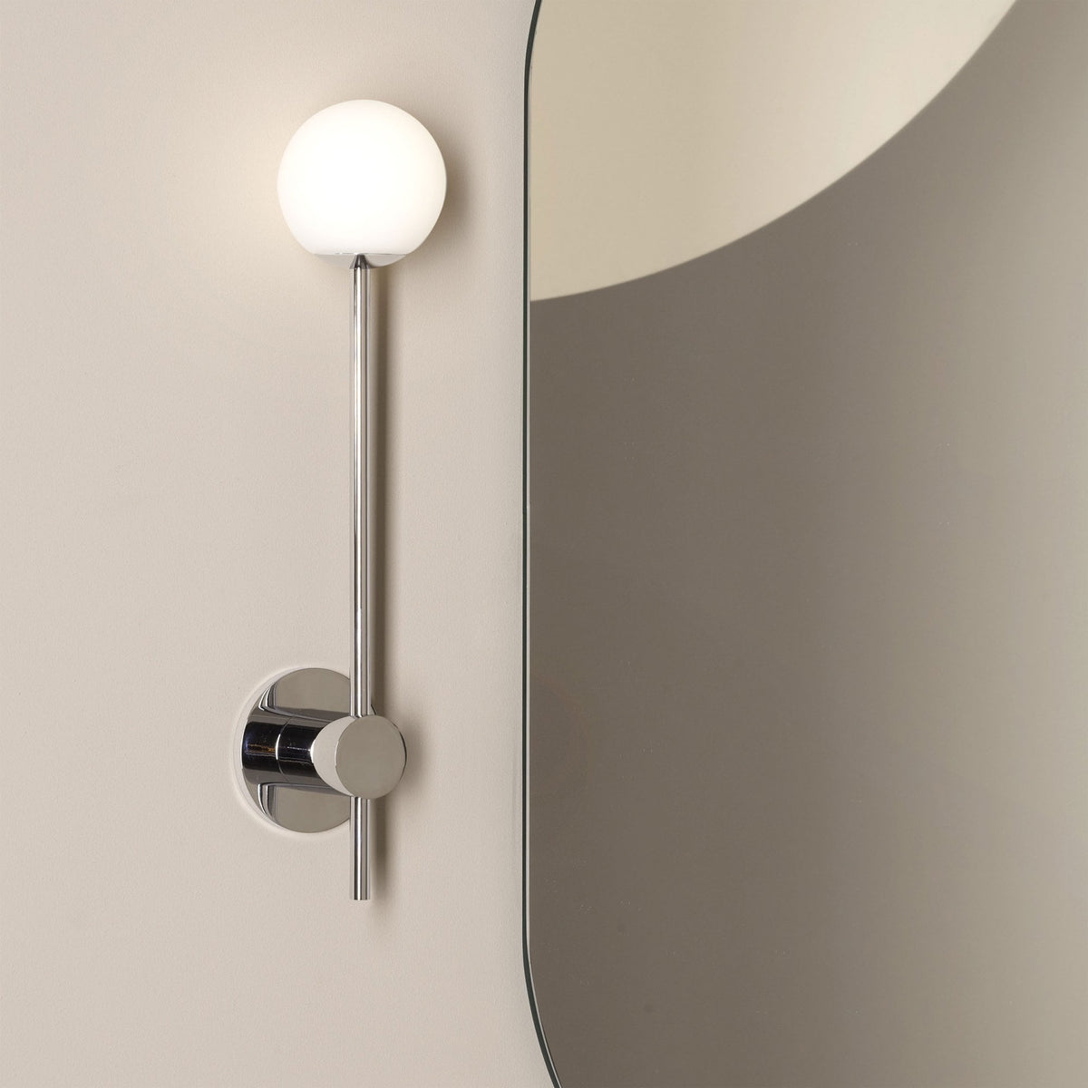 Chrome wall light with a spherical white glass shade next to a mirror