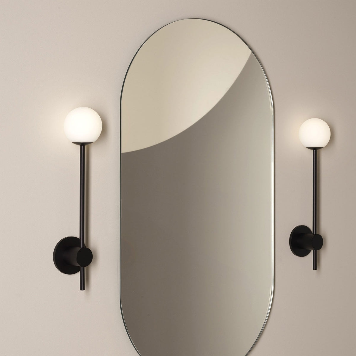 Two black wall sconces with spherical white lights flank a tall, rounded rectangular mirror