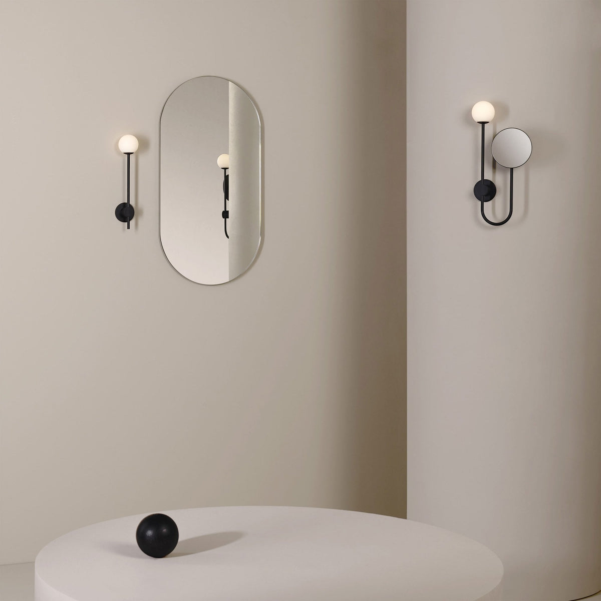 Two black wall sconces with spherical lights, one with an oval mirror, the other with a round mirror