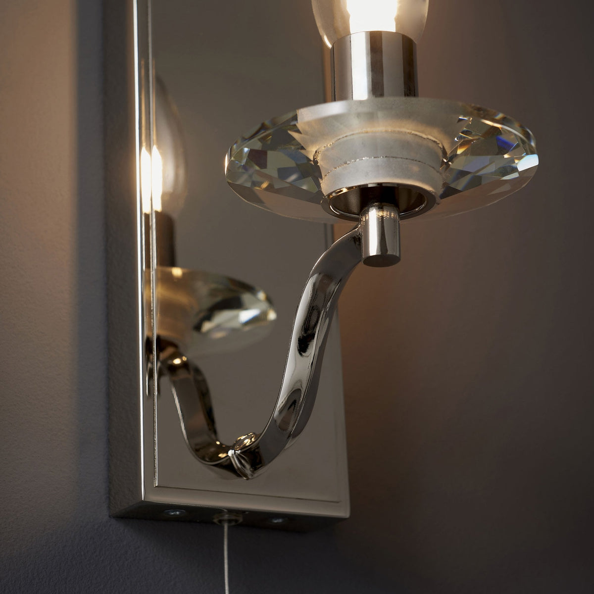 Close-up of a polished chrome wall light with a faceted clear glass candle holder and a mirrored backplate.