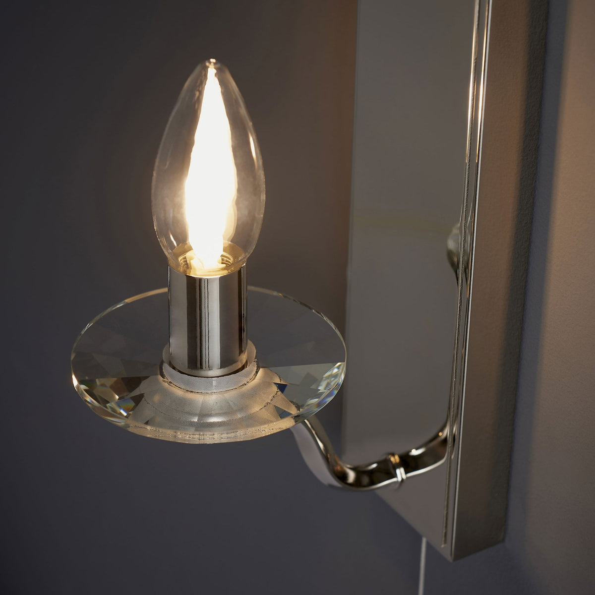 Angled view of a polished chrome wall light with a clear glass candle holder and a mirrored backplate.