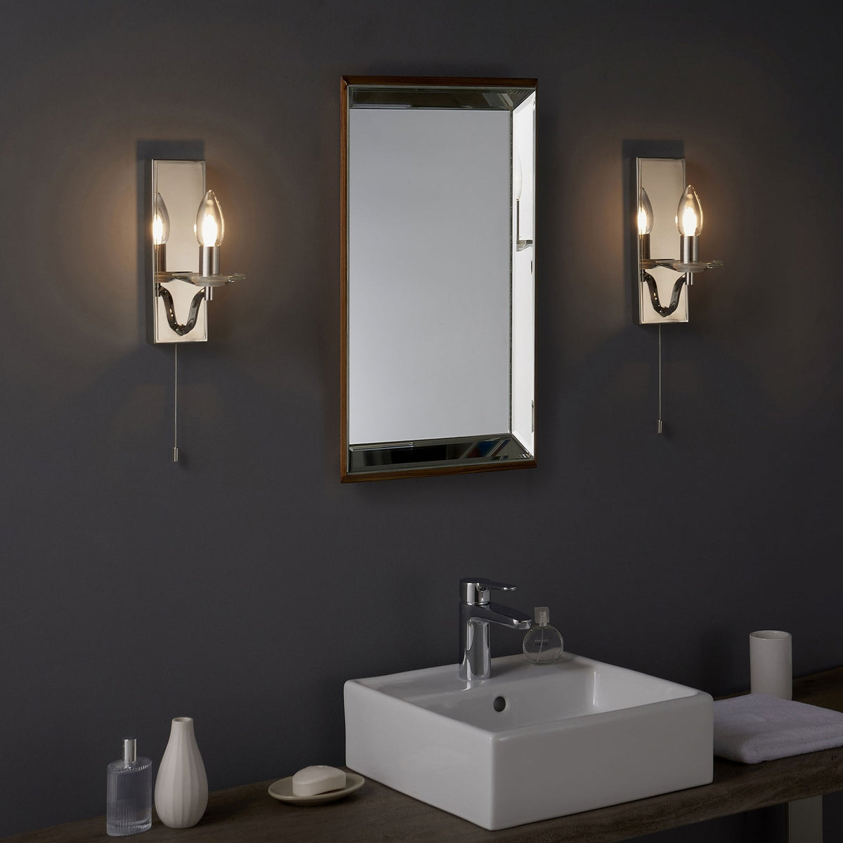 Two polished chrome wall lights flanking a mirror above a white sink in a modern bathroom.