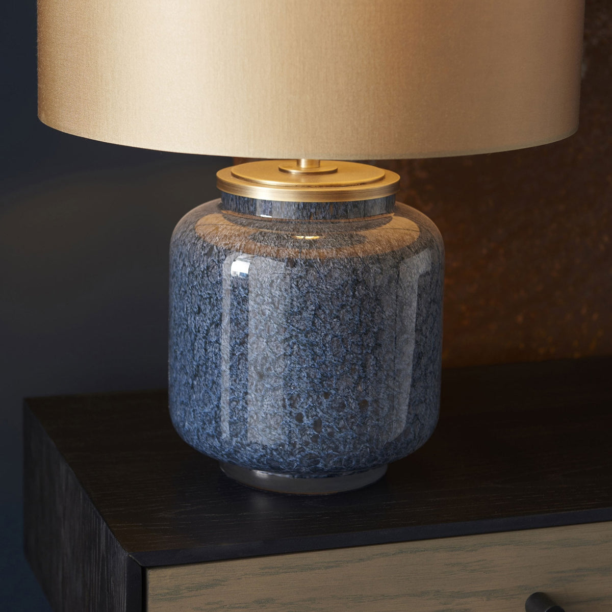 A close-up of the blue glazed table lamp with a gold lampshade on a wooden console table.