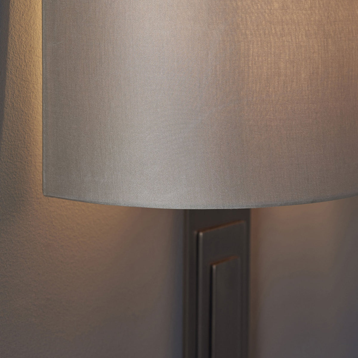 A close-up of a grey wall light with a textured shade and rectangular base, casting a soft light.