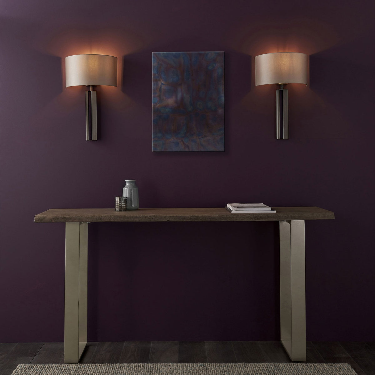Two modern wall lights illuminate a wooden console table with minimalist decor and abstract art.