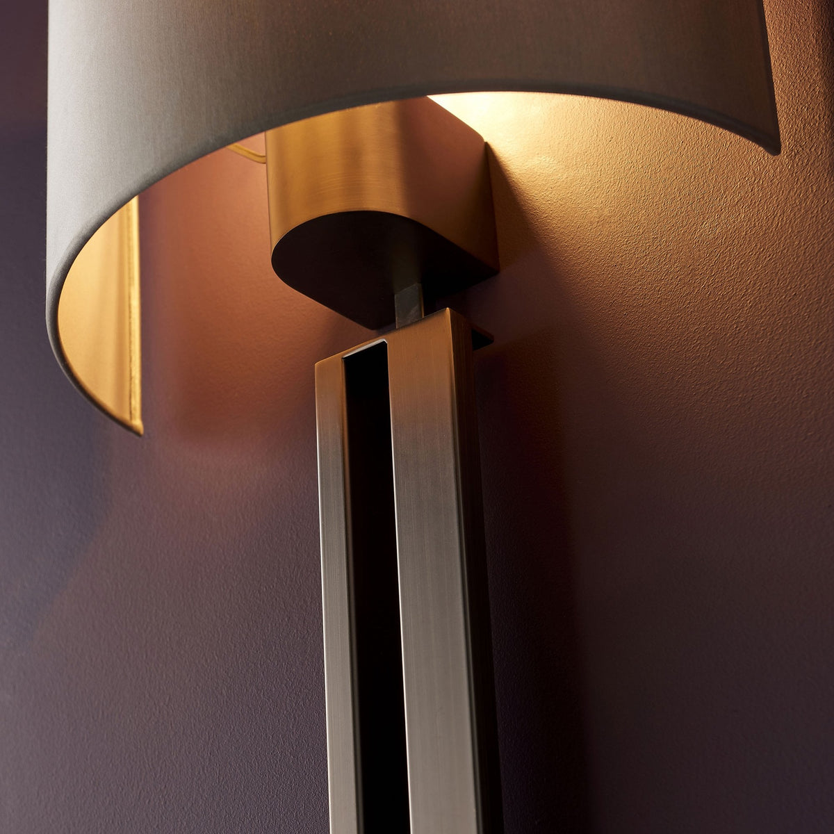 Detail of a modern wall light showing the bronze and dark metal components and a glowing interior.