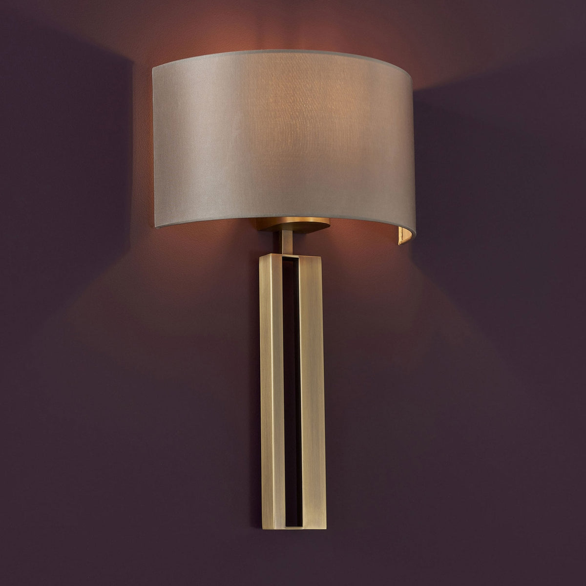 A close-up of a wall light with a rectangular brass base and a curved fabric shade.