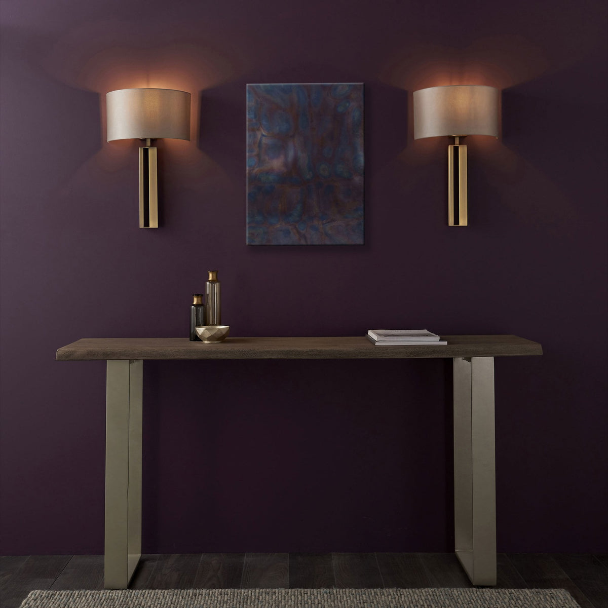 A console table with two brass wall lights and an abstract painting against a purple wall.