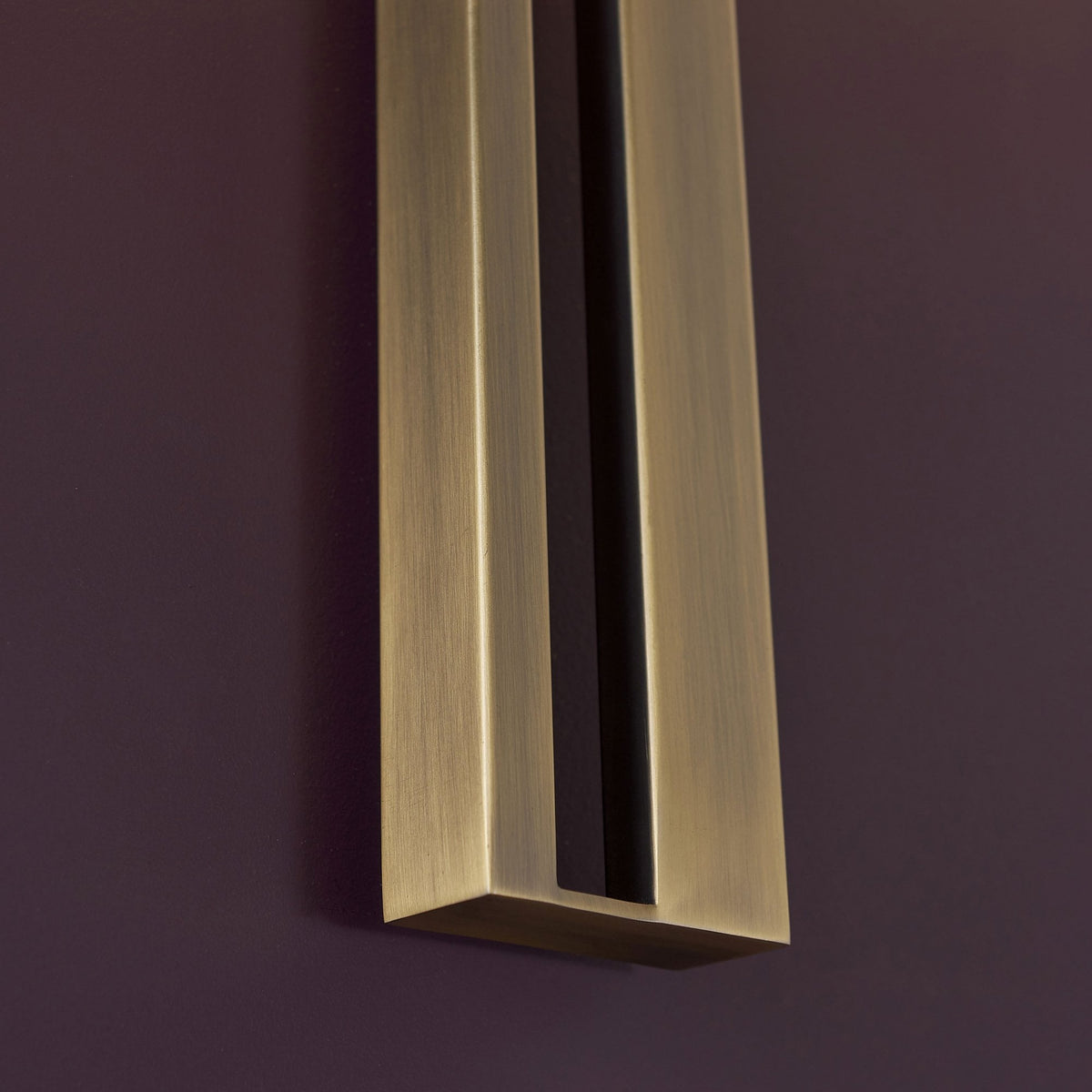 A close-up of the rectangular brass stem of a wall light, showing its textured finish.