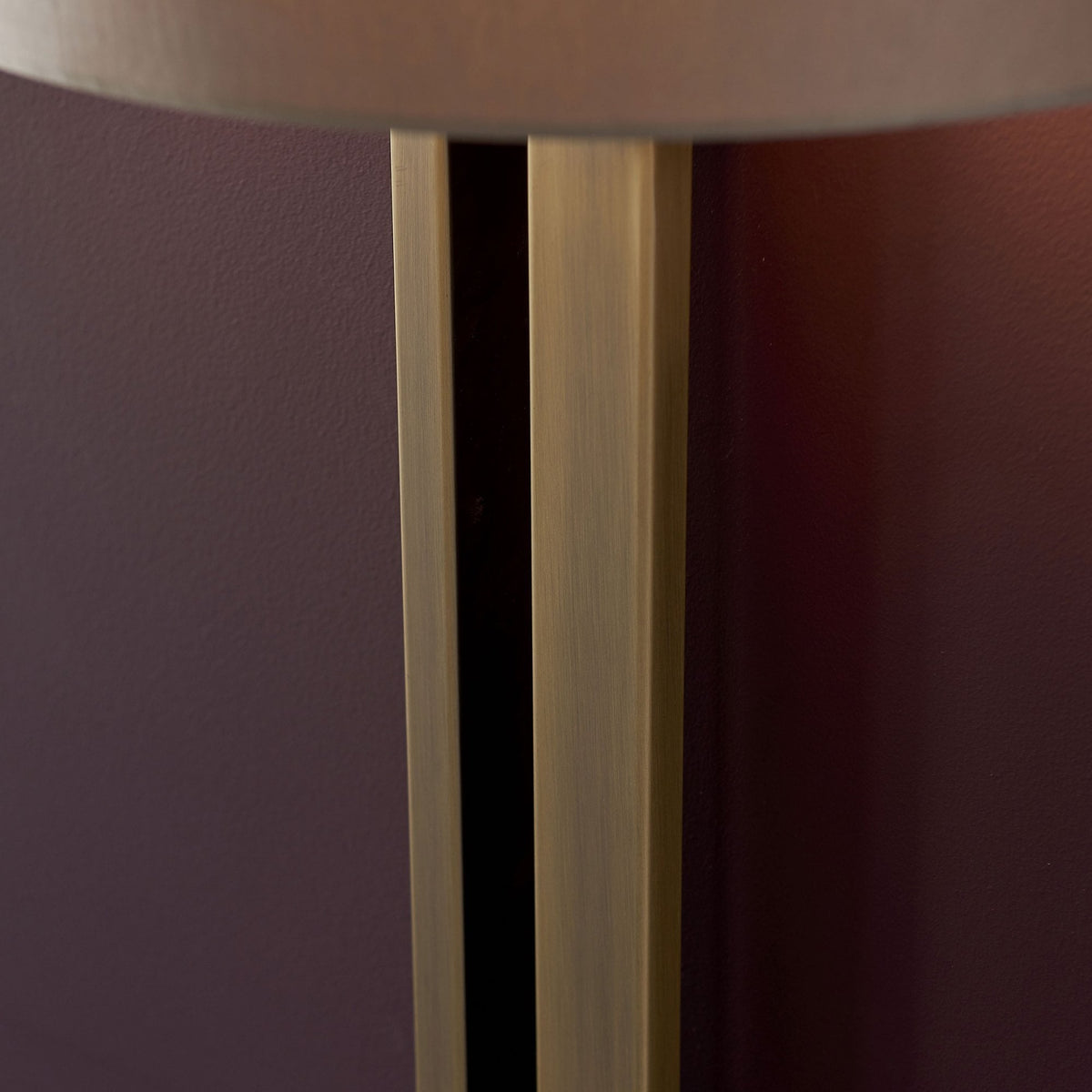 A close-up of the upper part of the brass stem and the bottom edge of the shade of a wall light.